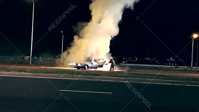 One firefighter dousing the burning vehicle with foam at the scene of the car crash