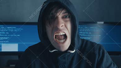 Portrait of Angry Hacker Programmer screams and shows aggression while working at the computer. Stress in the workplace.