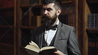 Intellectual elite concept. Old fashioned man reading a book at bookcase in library. Aristocrat on busy face with book