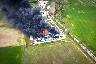 Aerial view of burnt industrial warehouse or logistics center building after big fire with huge smoke from burned roof
