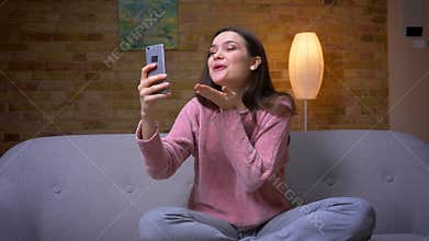 Closeup shoot of young pretty brunette caucasian female having a video call on the phone and smiling sitting on the