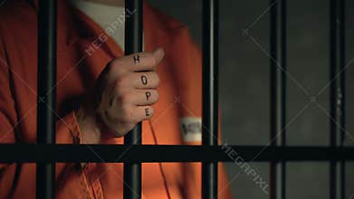 Hope word on imprisoned man fingers, holding jail bars, dream about freedom