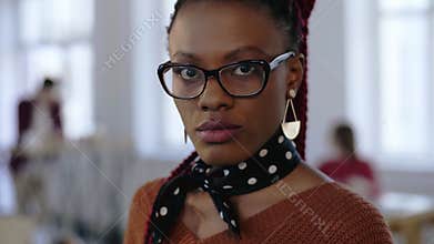 Close-up portrait of young beautiful serious black business woman in eyeglasses looking at camera at office workplace.