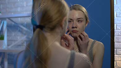 Crying teenager examining problem face skin looking in mirror at home, acne