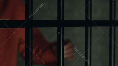 Criminal with beaten hands standing behind prison bars, conflicts in jail