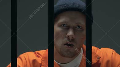 Confident bandit chewing toothpick behind prison bars, dangerous head of mafia