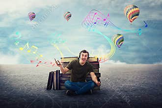 Joyful student guy seated relaxed on the floor listening to a song on headphones