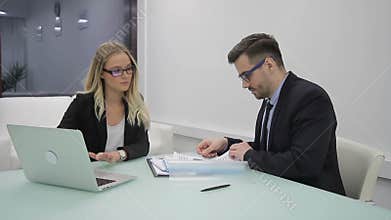 In office, a woman and a man are studying documents near laptop.