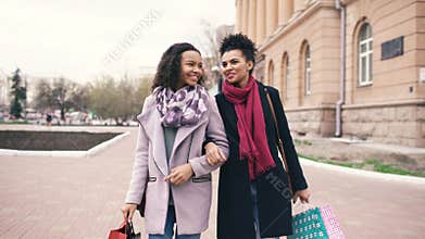 Two attractive mixed race women with shopping bags talking and walking down the street. Girlfriends have fun after