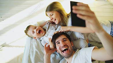 Smiling parents with baby taking selfie family photo on bed at home