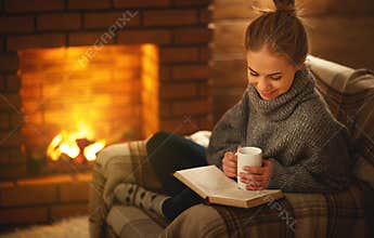 Young woman reading a book by the fireplace on a winter evenin