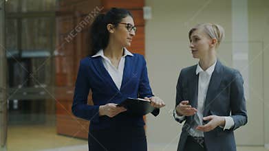 Two businesswomen colleagues discussing project while walking in modern office