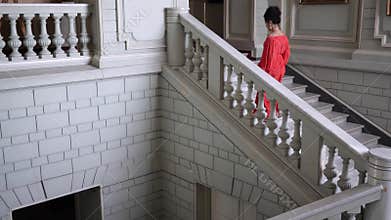 Singer in elegant red dress on high heels climbs a large staircase at beautiful hall