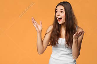 Surprised happy beautiful woman looking sideways in excitement, isolated on orange background