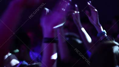 Crowd in night club is waving hands. Many people, teenagers are dancing to music