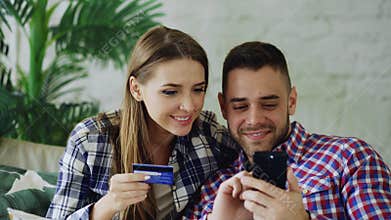 Attractive young couple with smartphone and credit card shopping on the internet sit on couch in living room at home