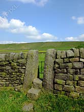 A dry stone wall with stone stile or narrow gate with steps in a yorkshire dales hillside meadow with a bright blue summer sky