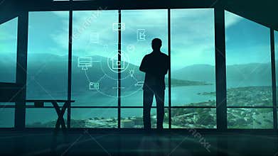 A man is standing by the window viewing IOT infographics elements