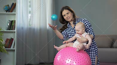 Responsible mother doing early development exercises with active baby girl