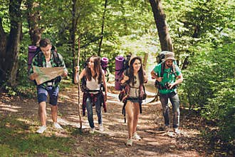Trekking, camping and wild life concept. Four best friends are hiking in the spring woods, the guy is checking the route on a map,