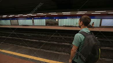Guy standing on empty platform in underground and waiting for a train to arrive