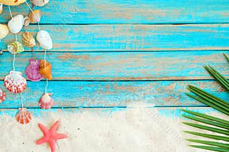 Summer background with beach sand, starfishs coconut leaves and shells decoration hanging on blue wooden background.