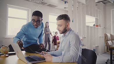 Two young multiethnic friends collaborate in stylish loft office, European female manager comes up to help them 4K.
