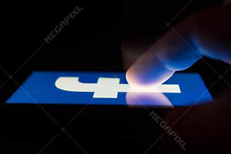MOSCOW, RUSSIA - May 9, 2018: A smartphone lying on a table in the dark, displaying the logo of the Facebook.