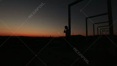 Silhouette of lonely thoughtful woman standing on the high-tech bridge on red sunset