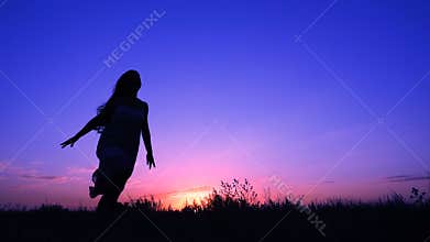 Silhouette of young girl running against pink sky