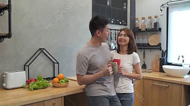 Beautiful happy asian couple are drinking a cup of coffee together in the kitchen. Man and woman talking while having breakfast.