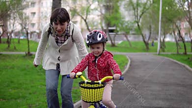 Mother teaches little daughter to ride a bicycle.