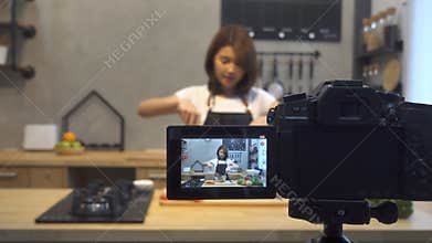 Young asian woman in kitchen recording video on camera. Smiling asian woman working on food blogger concept.