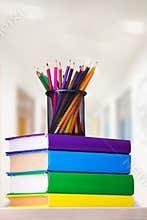 Glass with colored pencils on a stack of books on a table, school concept