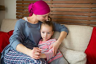 Young adult female cancer patient spending time with her daughter at home, relaxing on couch. Cancer and family support concept.