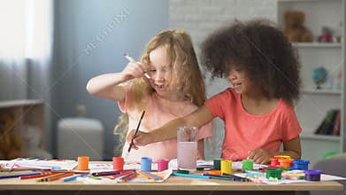 At kindergarten, two positive multiracial girls painting with watercolors, hobby