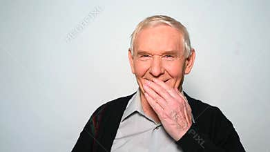 Funny old man laughs covering mouth with hand.