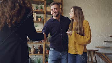 Slow motion of housing agent giving keys to buyers of new apartment, happy husband and wife are hugging and kissing, man