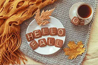 Autumn cozy flat lay. Top view. Hot tea cup and round white plate with cookies text HELLO FALL, orange warm scarf and autumn leav