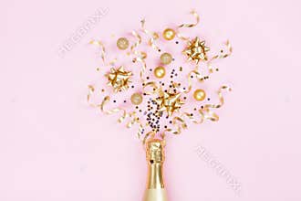 Champagne bottle with christmas decoration from confetti stars, golden balls and party streamers on pink background. Flat lay.