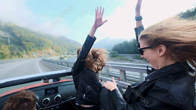 Two beautiful young girls ride in a red cabriolet among the mountains. Road on the highway. Dressed in black leather