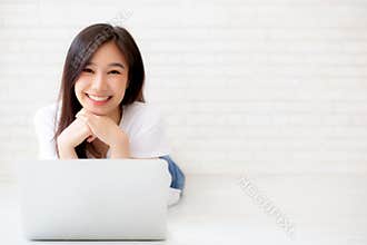 Beautiful of portrait asian young woman working online laptop lying on floor brick cement background, freelance girl using