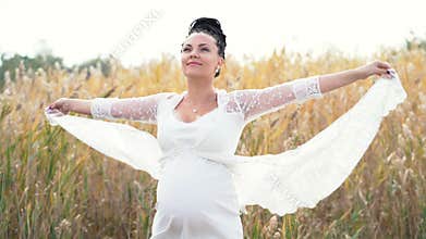 Beautiful pregnant woman on nature background. Girl holds edges of her long lace dress that flutters in wind. Lady have