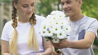 Boy giving flowers to pretty girl, pleasant surprise, first love in adolescence