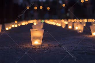 A group of candles burning in street and people holding candles in the background. Day of Memory of the Bereaved