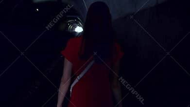 Back view of woman walk alone in tunnel at night. Scared female run fast from her pursuer at night