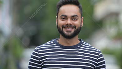 Young happy bearded Indian man smiling outdoors