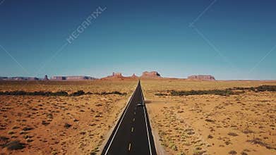 Drone follows silver car driving along famous sunny American desert highway road in Monuments Valley in Arizona and Utah