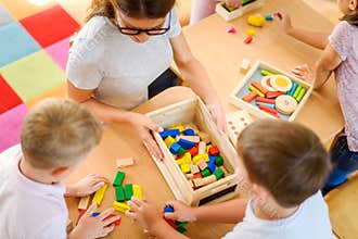 Preschool teacher with children playing with colorful didactic toys at kindergarten