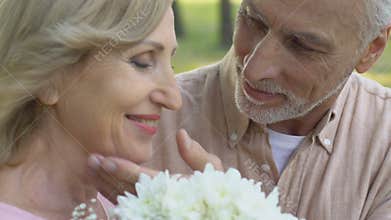 Old man bringing bouquet of flowers to woman and hugging her tenderly with love